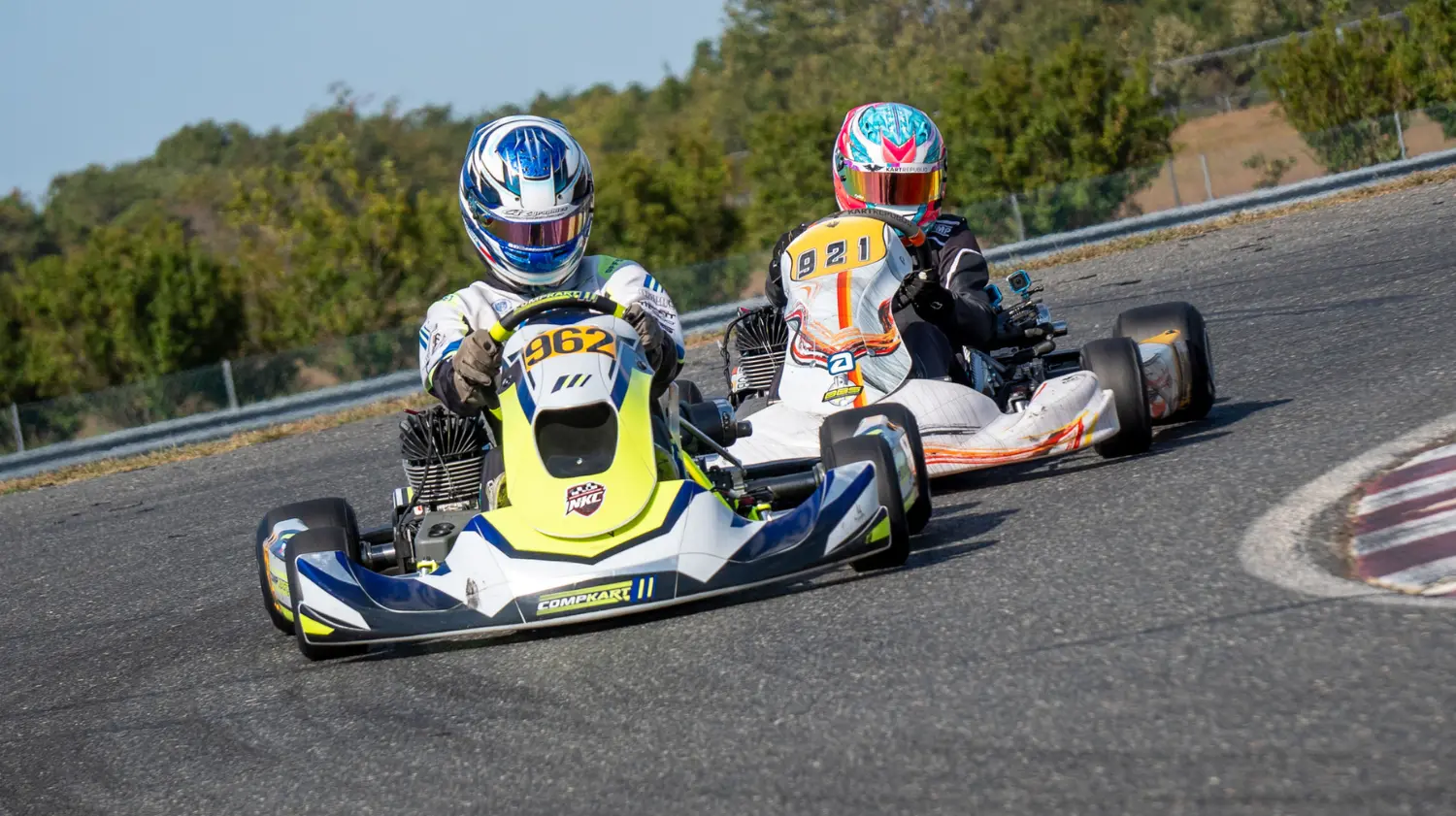 Two kart racers battling side by side through a corner during an outdoor LO206 sprint karting race